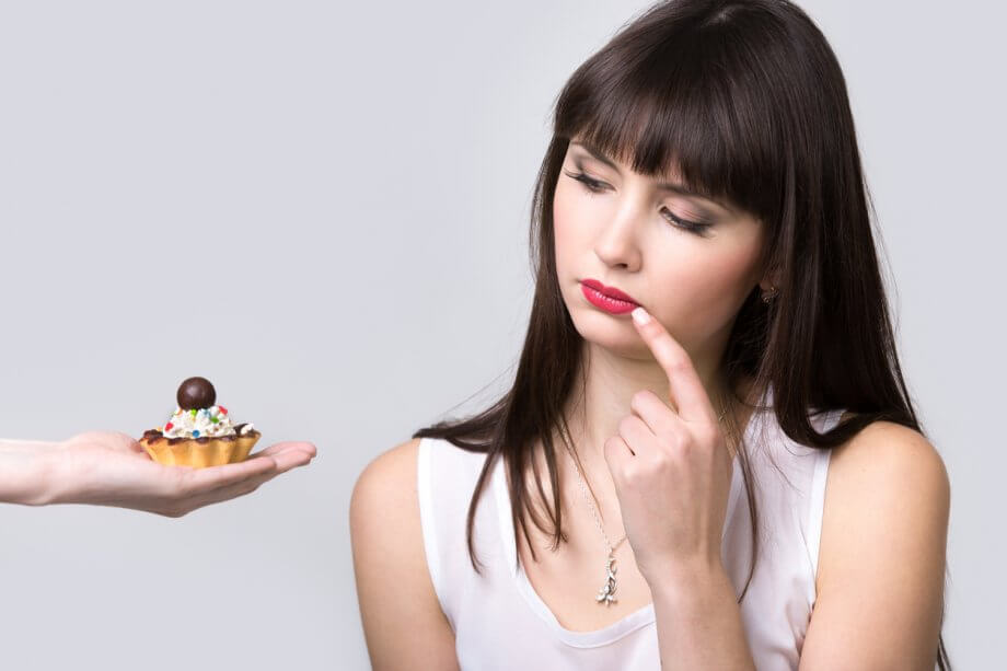 Woman with long black hair being offered a sweet and considering whether or not to eat it.